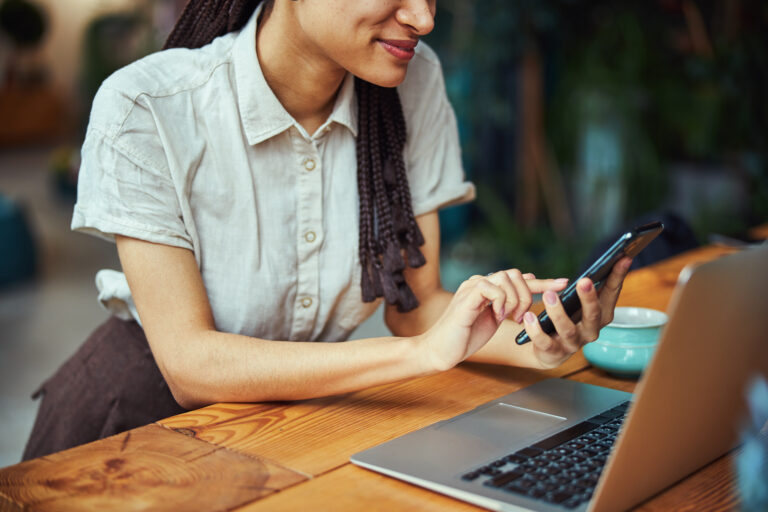 woman with long hair looking at her phone and her laptop is open